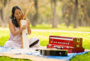 Woman playing an instrument with strings in the park, sitting on a blanket.